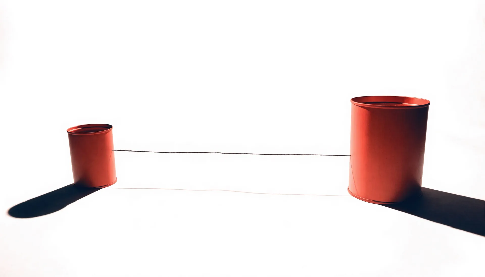 Conceptual still life: two objects held apart on a studio sweep, joined by one taut coral line.